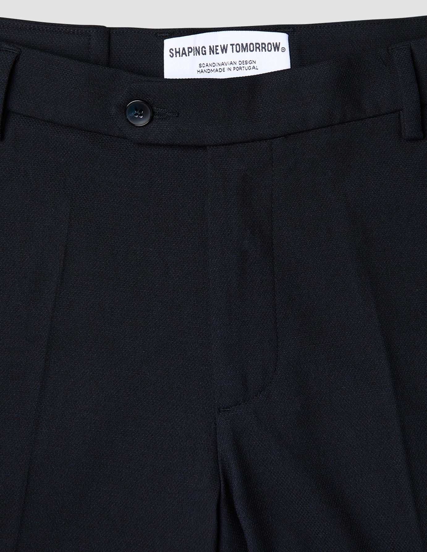 Nahaufnahme einer atmungsaktiven, dunkelblauen Motion Suit-Hose in Regular-Passform in Mitternachtsblau mit 360°-Stretch, Knopfverschluss und einem Innenetikett mit der Aufschrift Shaping New Tomorrow, Scandinavian Design und Handmade in Portugal.